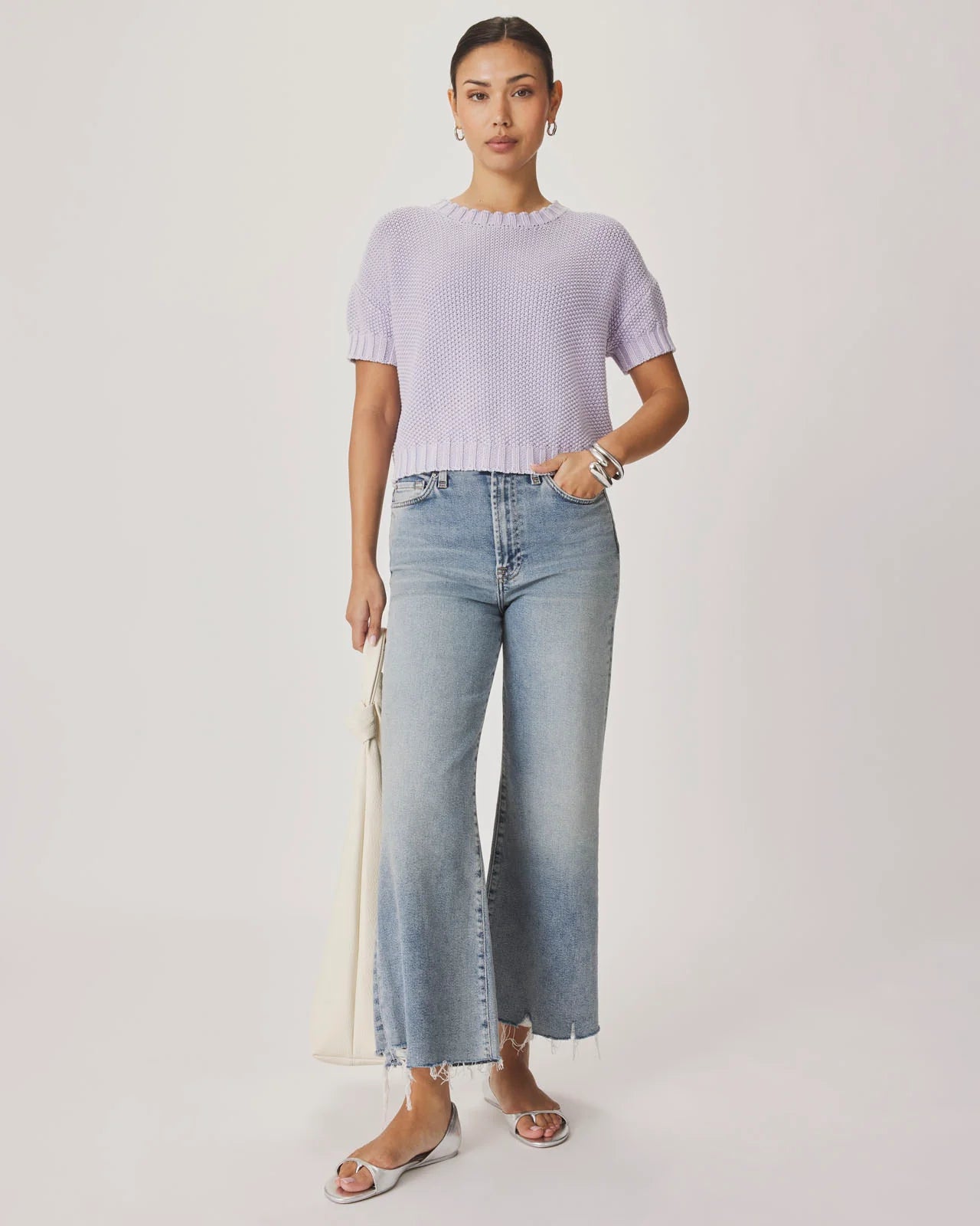 Woman wearing a light purple sweater and blue jeans against a white background