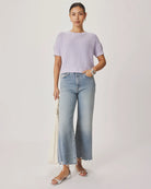 Woman wearing a light purple sweater and blue jeans against a white background