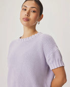 Woman wearing a light purple knitted sweater against a plain background