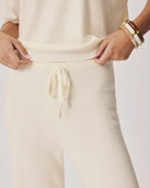 Person wearing a cream-colored outfit with a drawstring waistband on a plain background