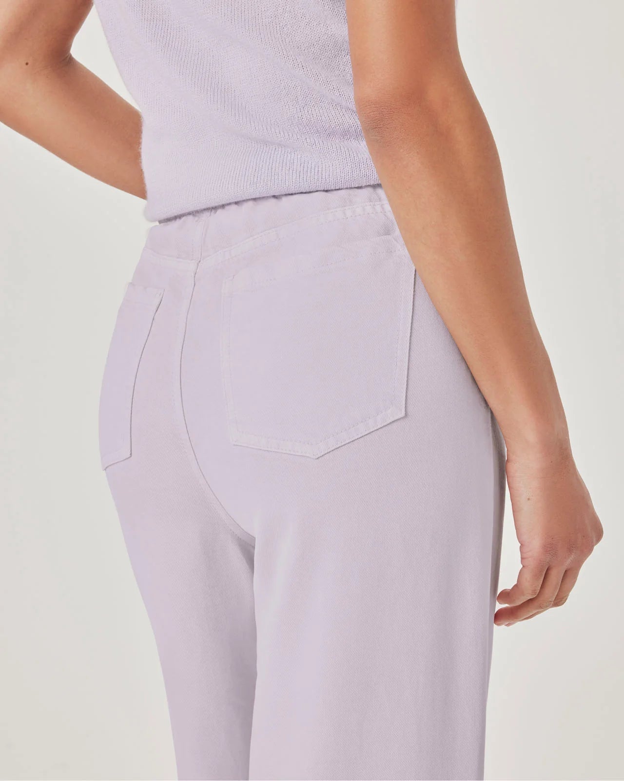 Person wearing light purple pants and a matching top on a plain background