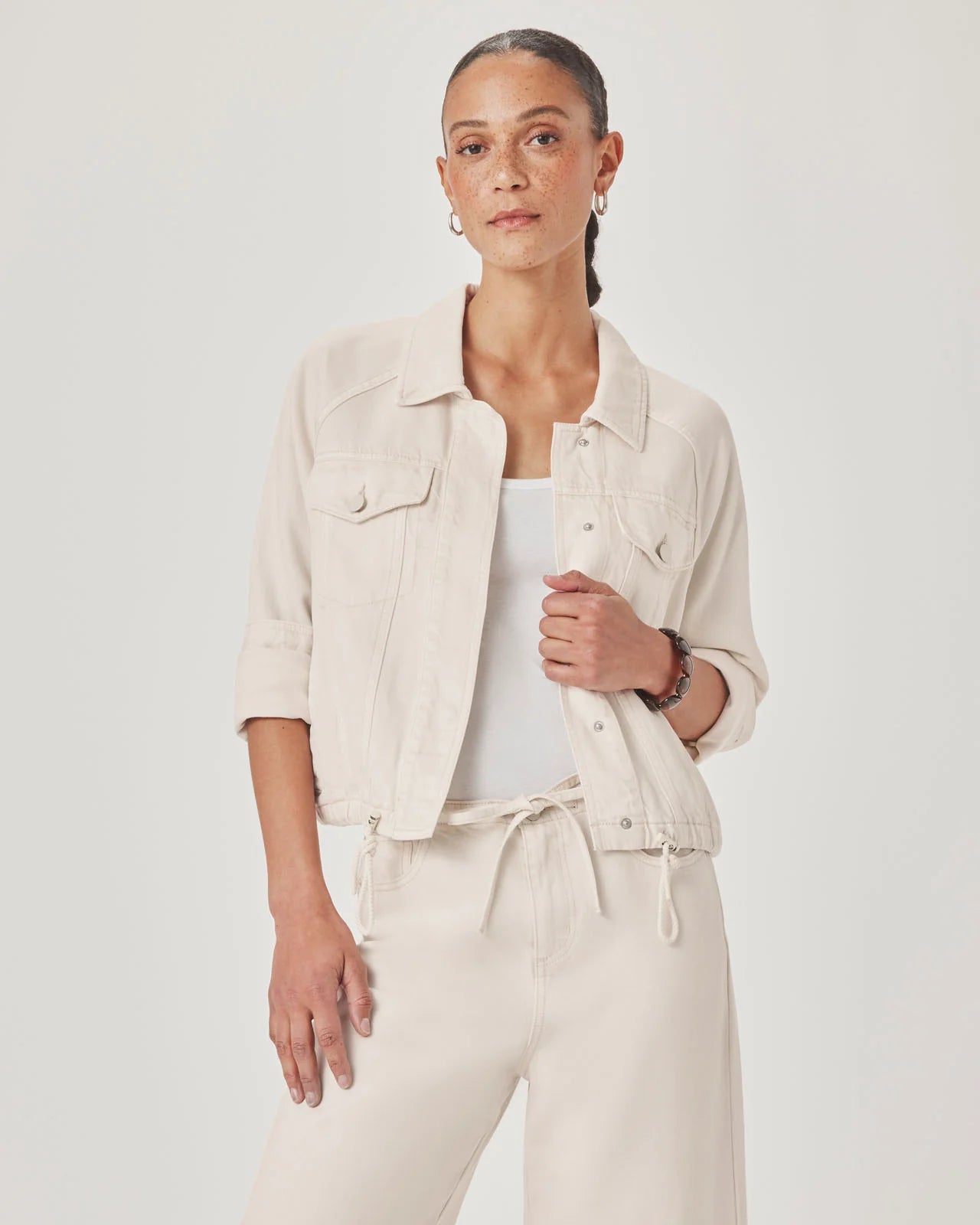 Woman wearing a beige jacket over a white top and pants on a light gray background
