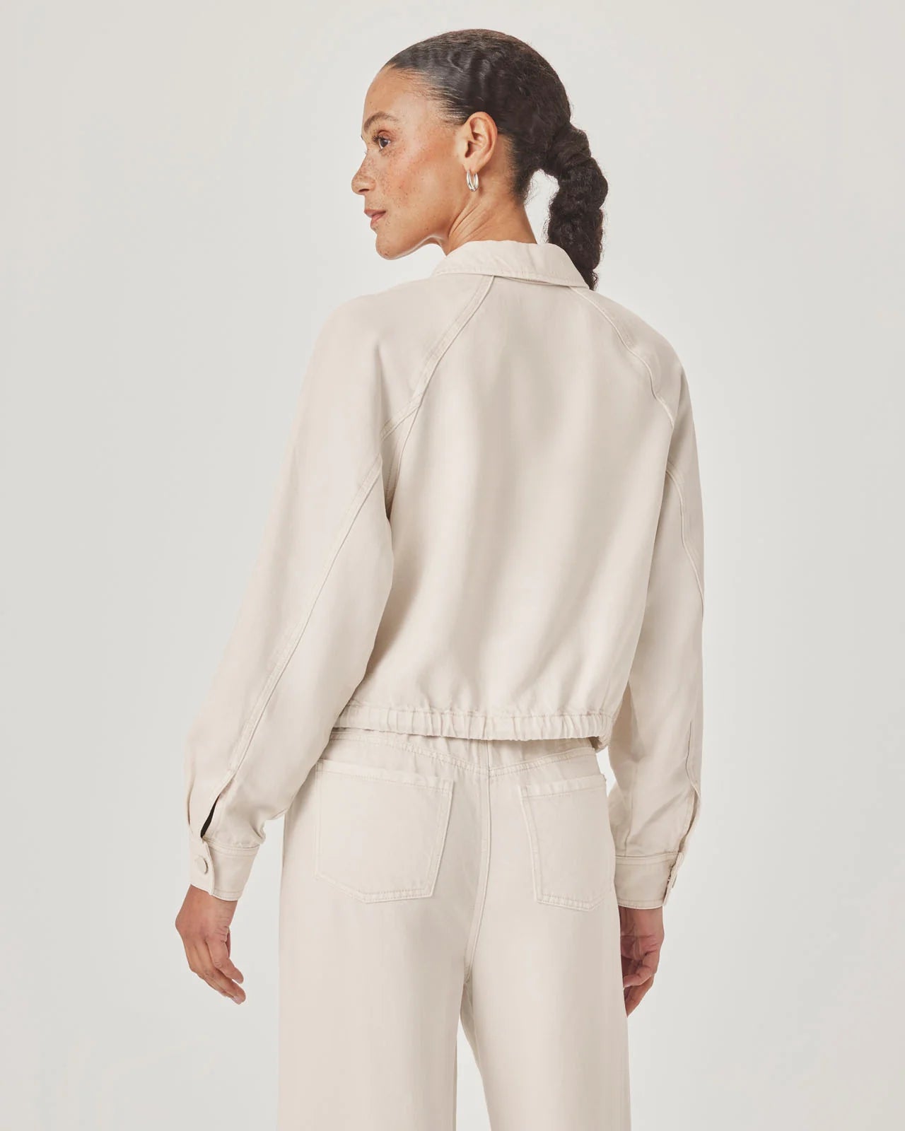 Woman wearing a beige jacket and pants on a plain background