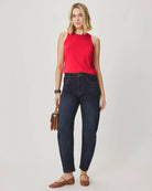 Woman wearing a red sleeveless top and dark blue jeans on a plain background