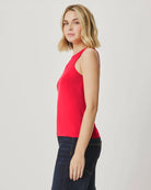 Woman wearing a red sleeveless top and dark jeans on a light gray background