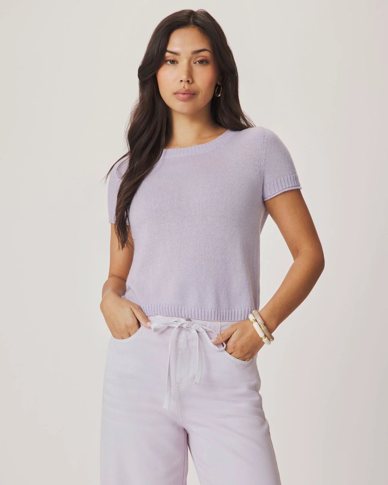 Woman wearing a light purple sweater and pants on a plain background