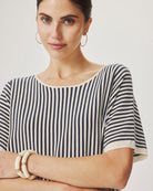 Woman wearing a black and white striped shirt with gold bracelets on a plain background