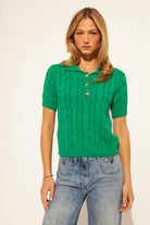 Woman wearing a green cable knit sweater and blue jeans on a white background