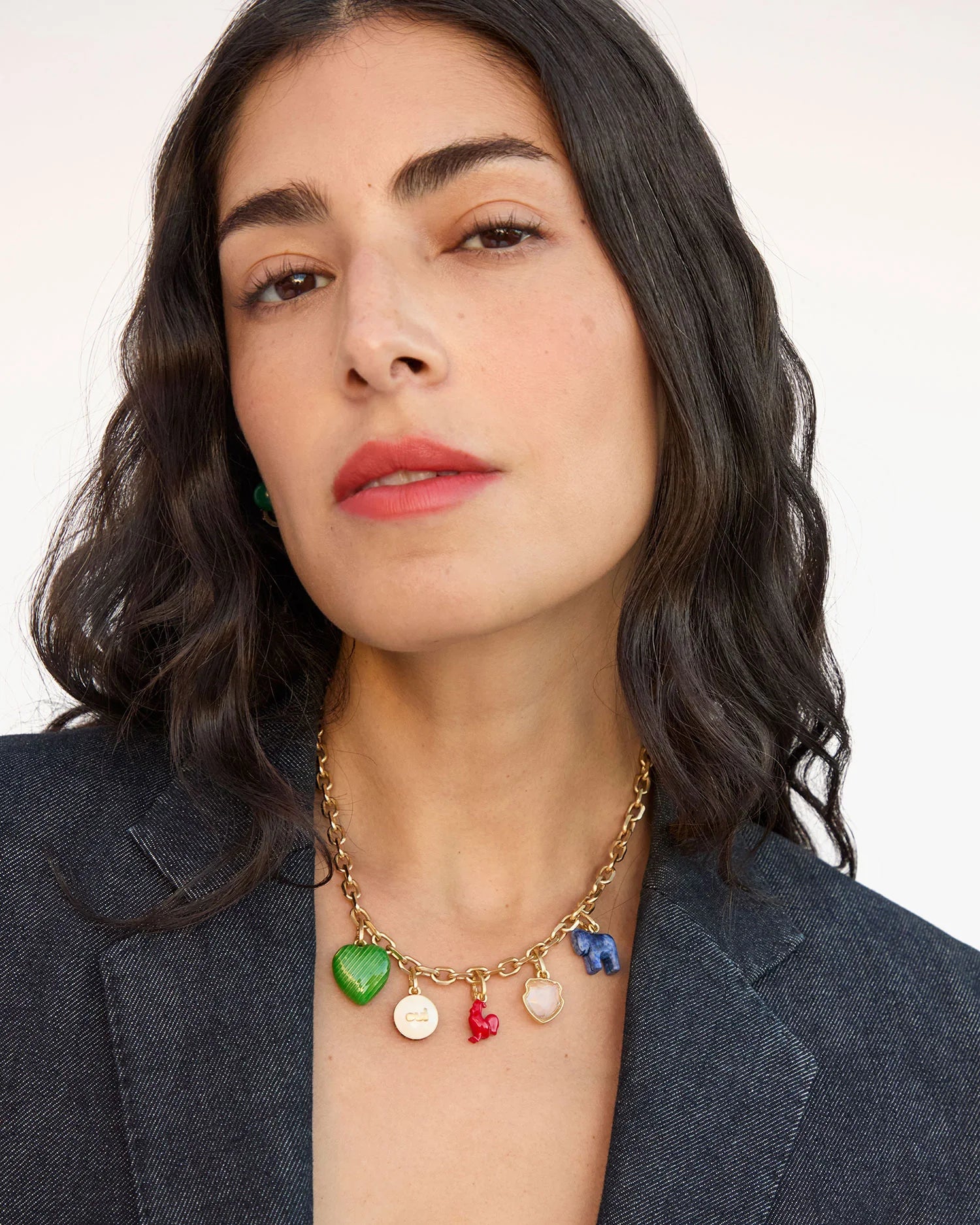 Woman wearing a gold necklace with colorful charms against a plain background