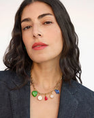 Woman wearing a gold necklace with colorful charms against a plain background