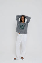 Person wearing a gray hoodie with a graphic design and white pants on a light gray background
