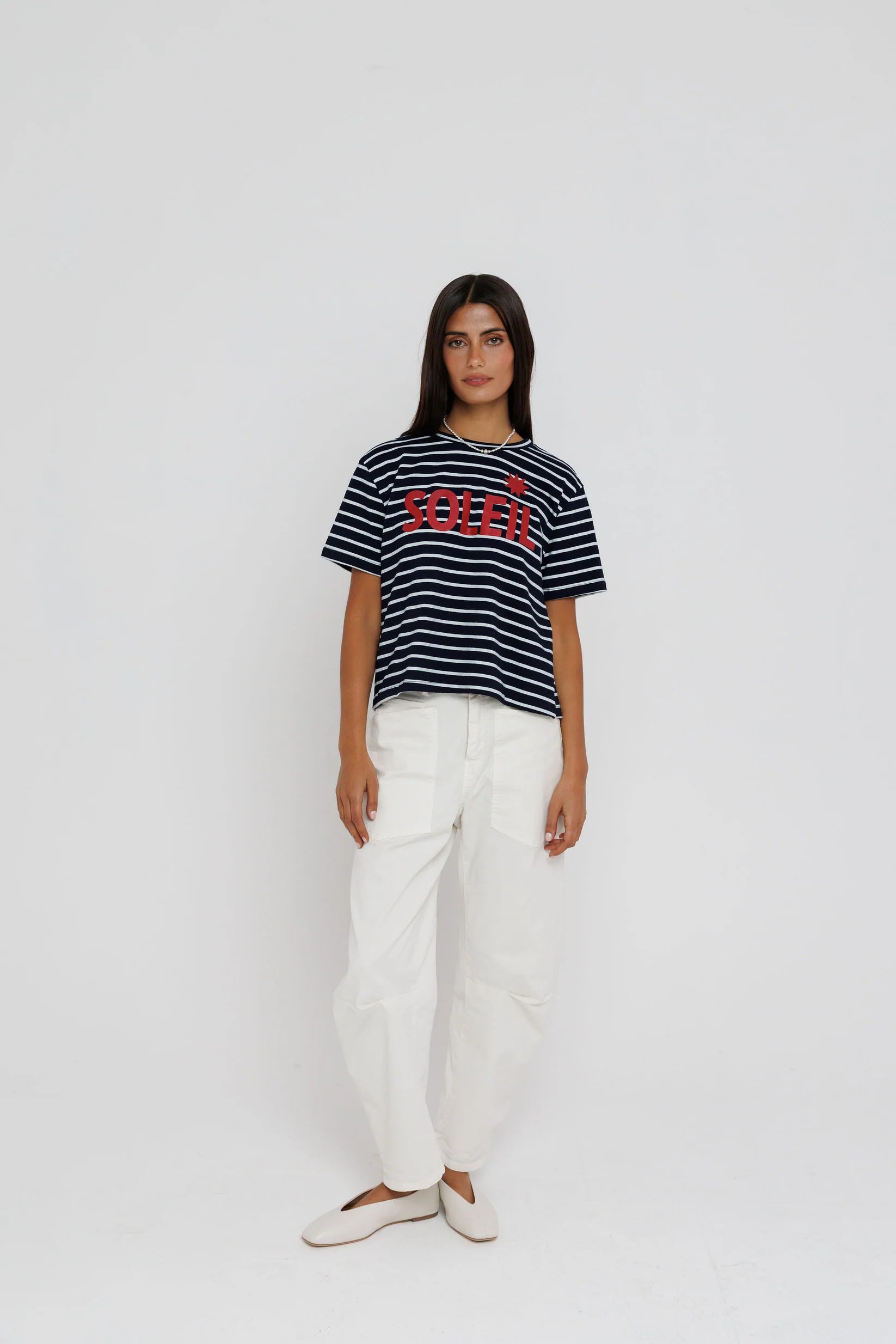 Person wearing a striped t-shirt with a logo and white pants on a plain background