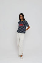 Person wearing a striped shirt with a logo and white pants on a plain background