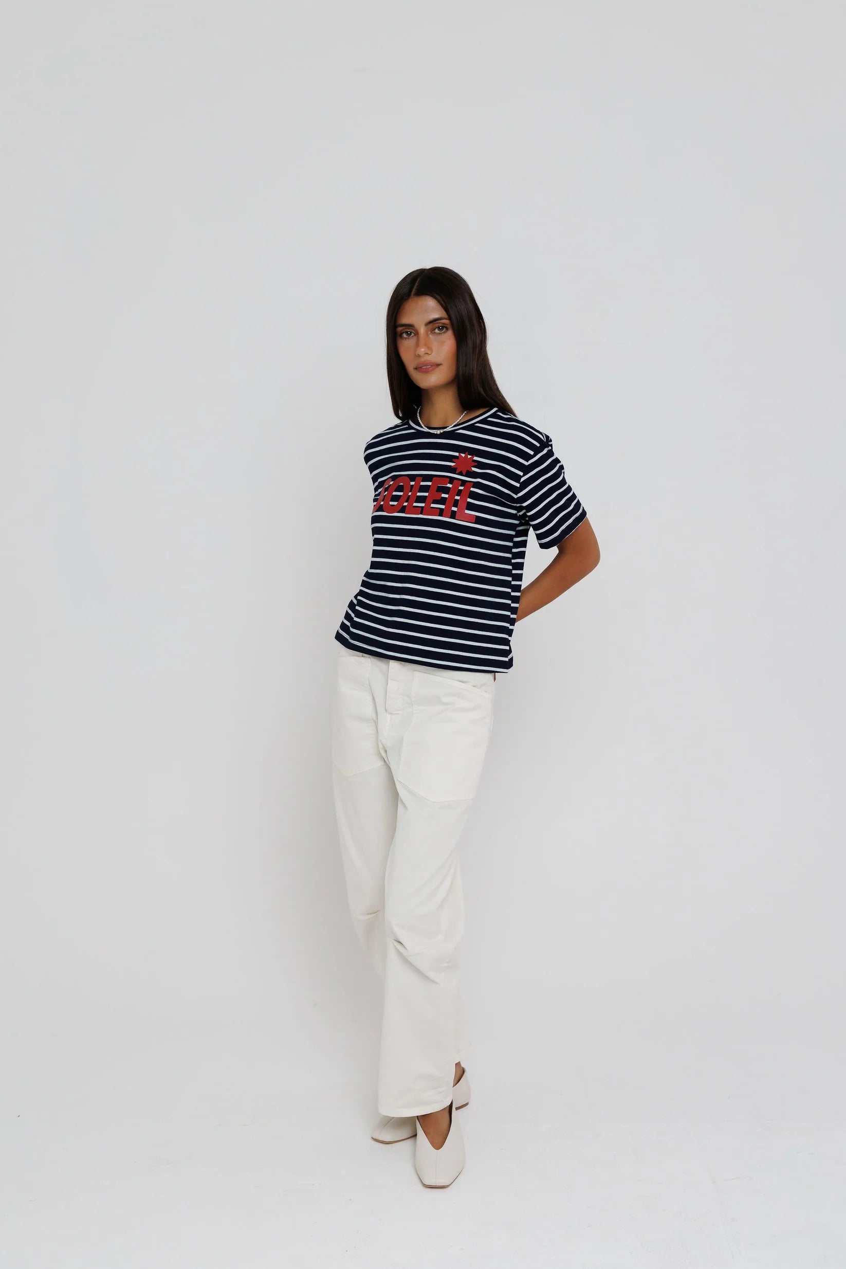 Person wearing a striped shirt with a logo and white pants on a plain background