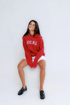 Woman wearing a red 'LOCAL' sweatshirt sitting on a white background