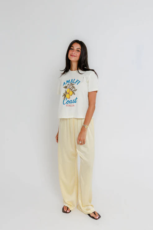 Woman wearing a white t-shirt with text and graphics, paired with light-colored pants on a plain background