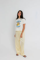 Woman wearing a white t-shirt with text and graphics, paired with light-colored pants on a plain background