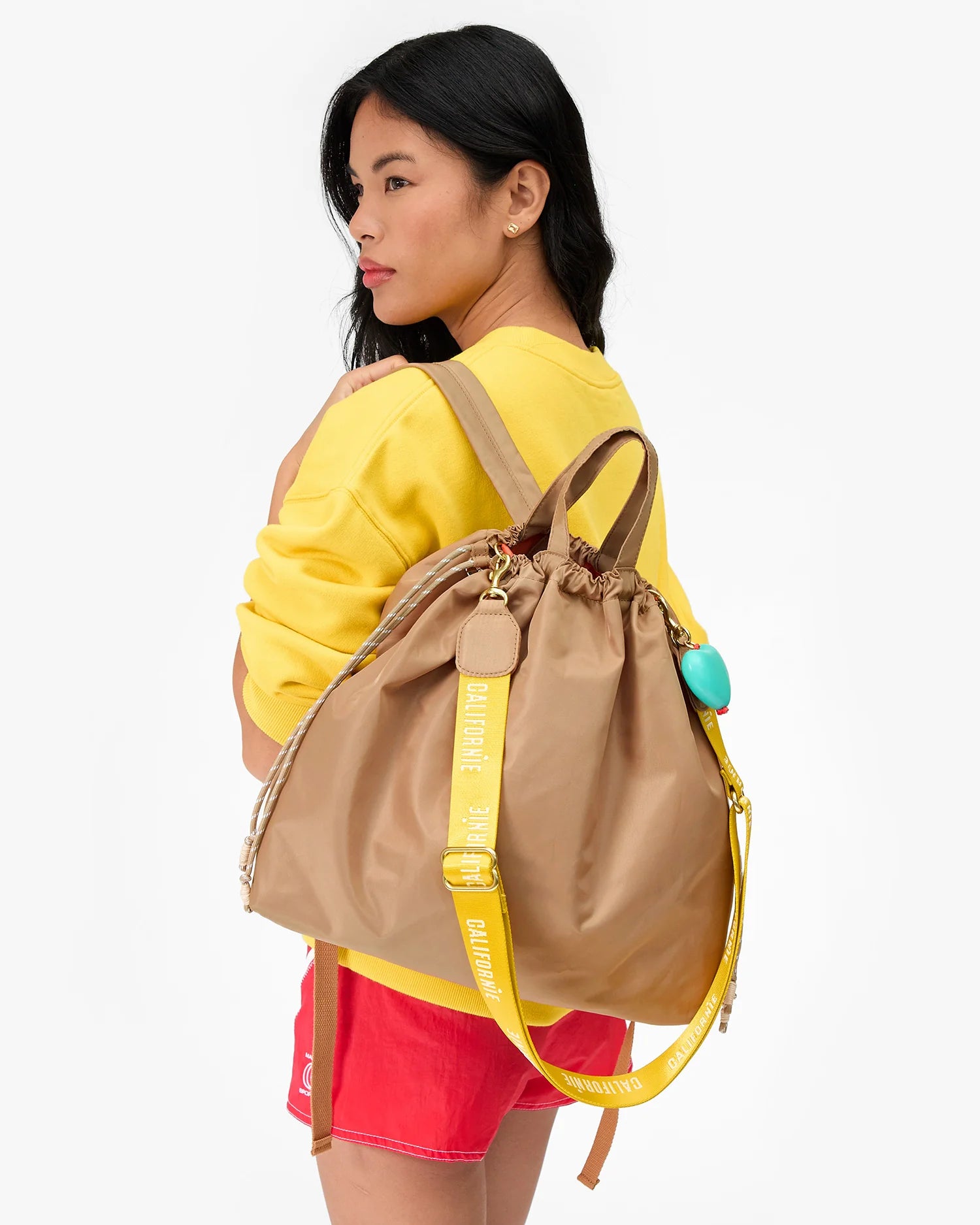 Woman wearing a beige backpack with yellow accents on a white background