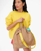 Woman holding a beige bag with a yellow strap against a white background