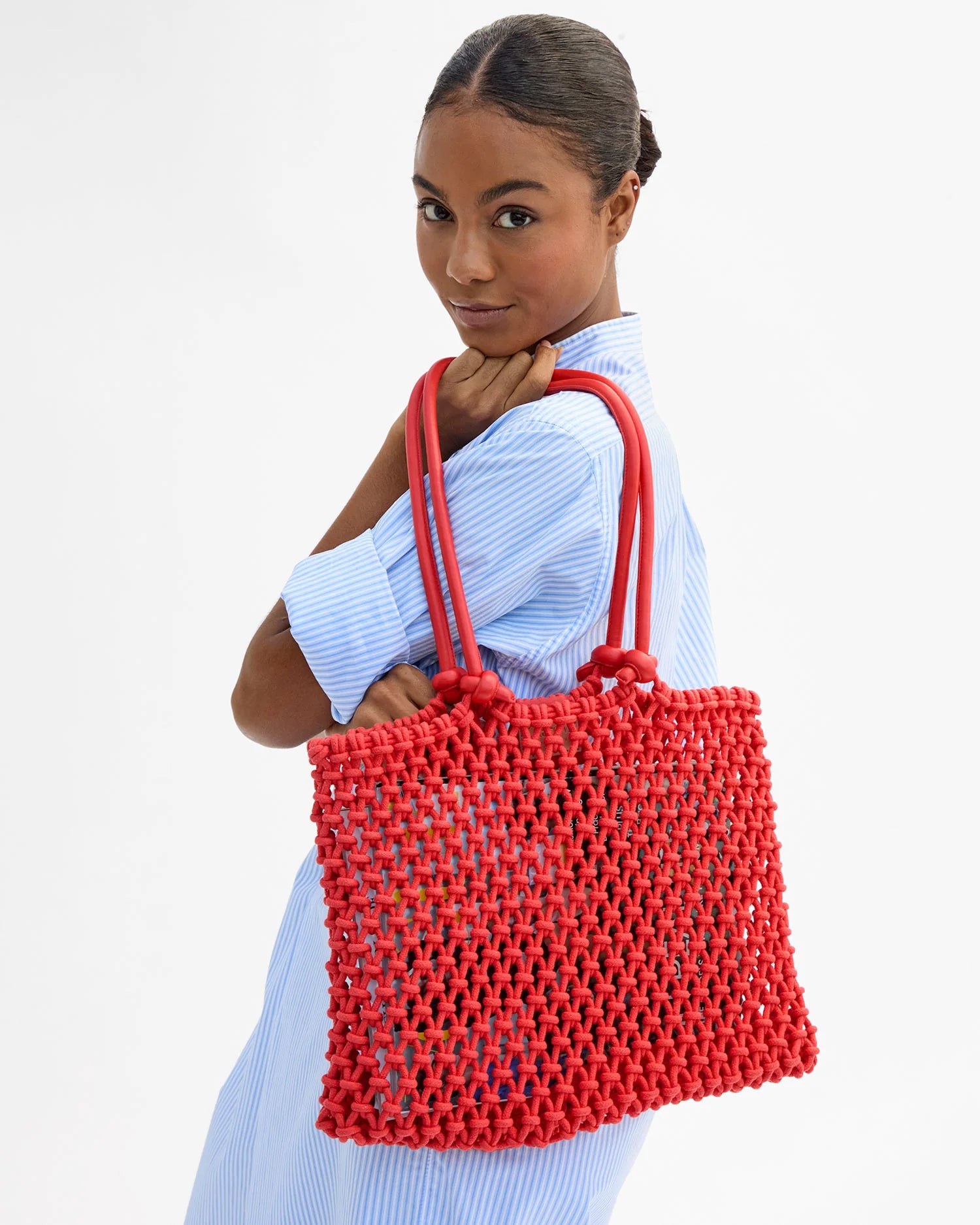 Woman holding a red woven handbag against a white background