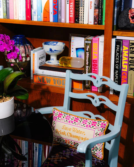 Chair with a colorful cushion in front of a bookshelf filled with books and decorative items.