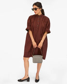 Woman wearing a brown dress with a checkered handbag on a white background