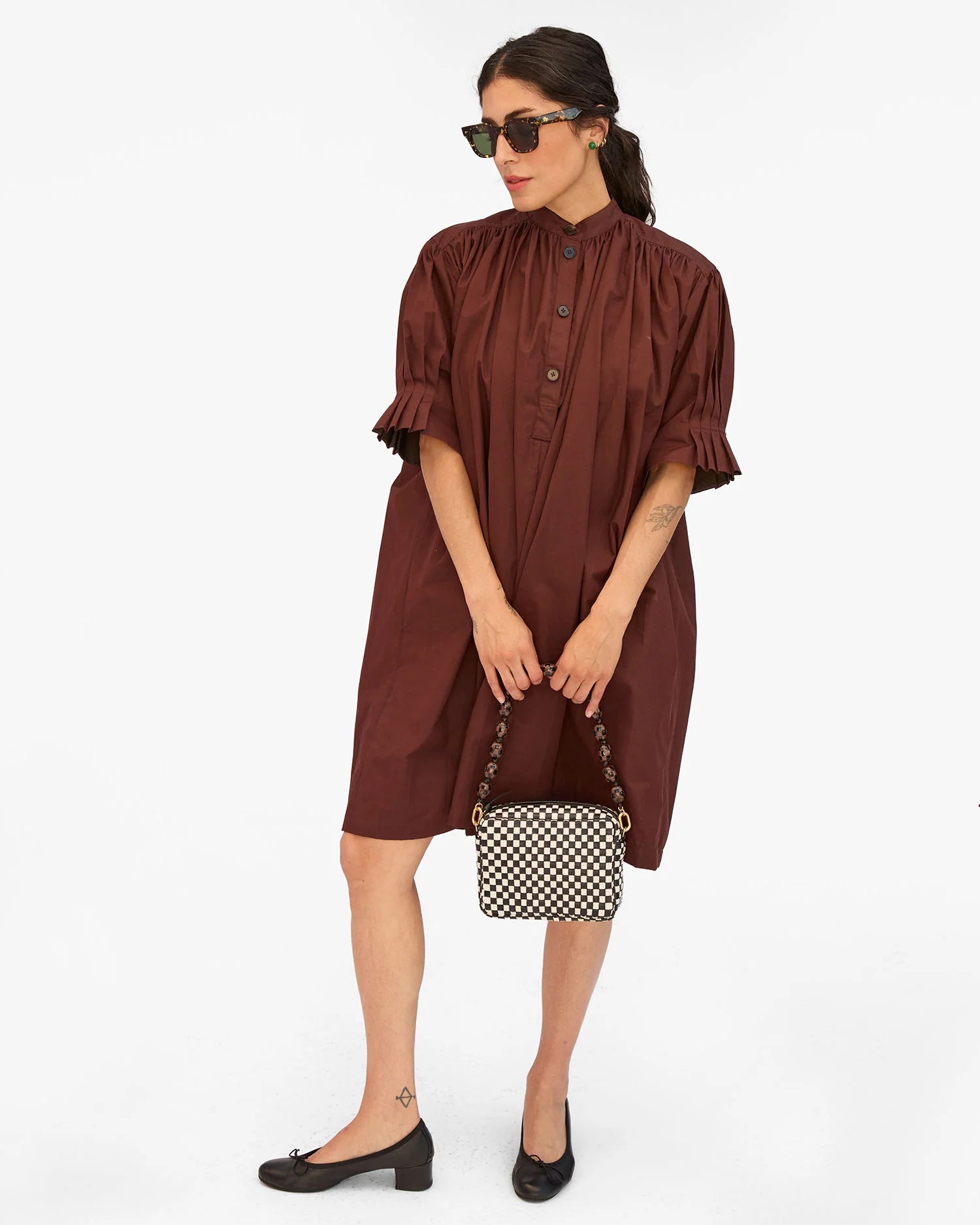 Woman wearing a brown dress with a checkered handbag on a white background