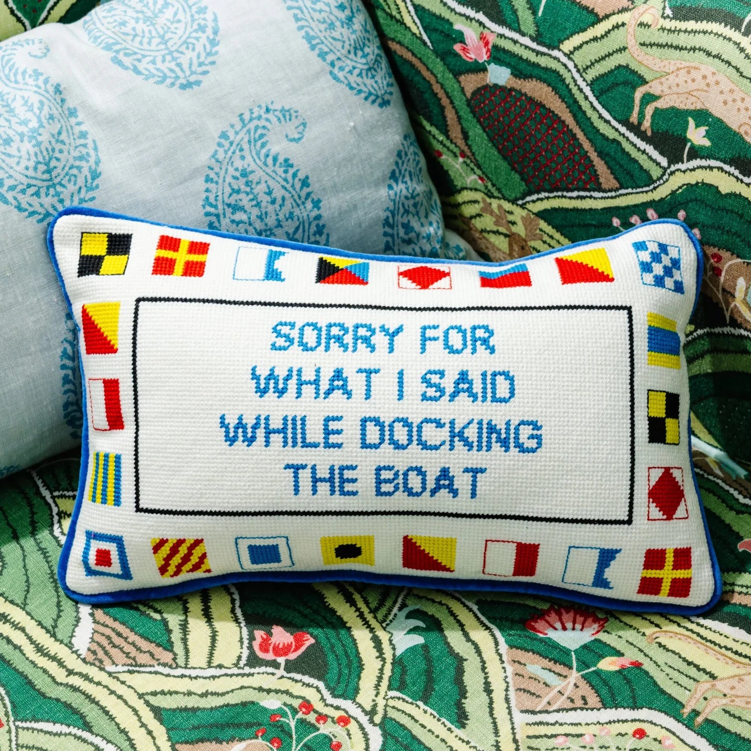 Decorative pillow with nautical-themed text and flags on a patterned fabric background