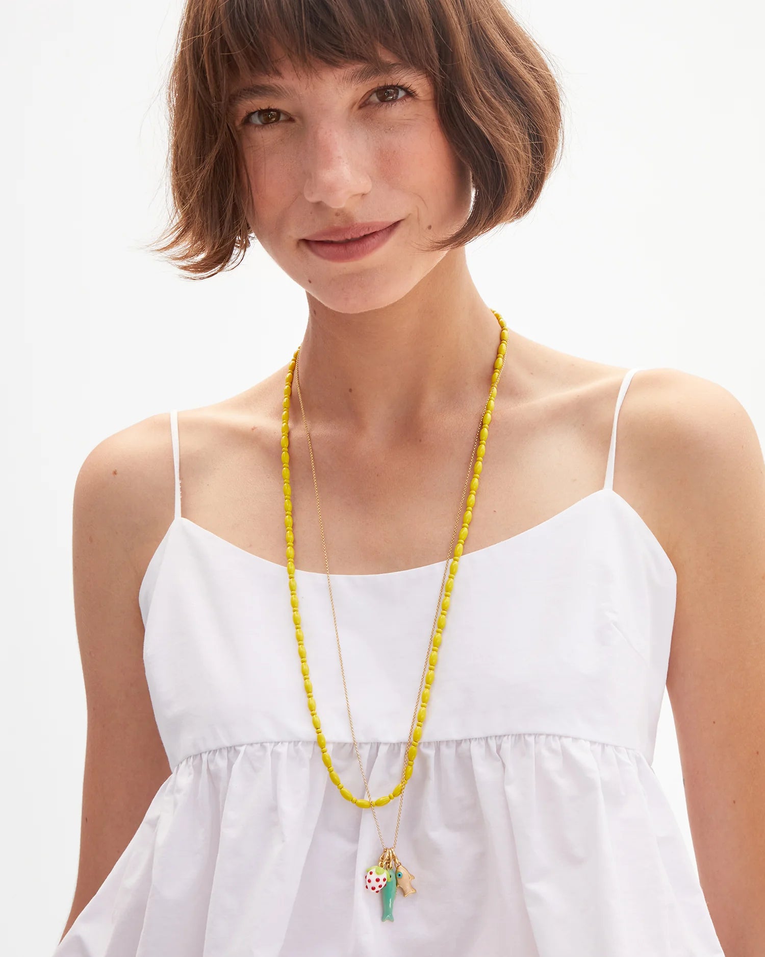 Woman wearing a white dress and yellow beaded necklace with a green pendant on a white background
