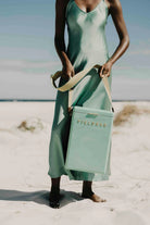 Woman in a green dress holding a matching 'Field & Co.' cooler on a beach.