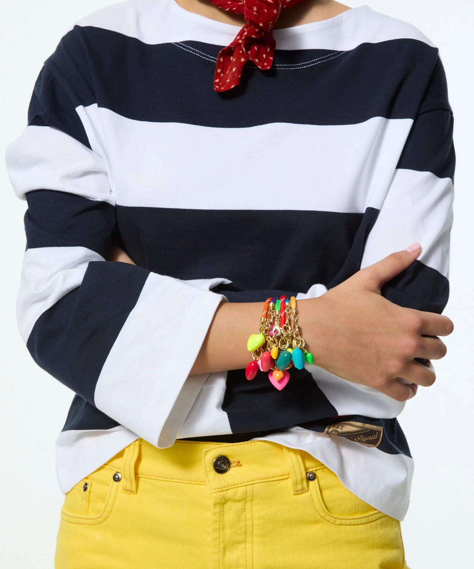 Person wearing a navy and white striped shirt with yellow pants, colorful bracelets, and a red polka dot headscarf.