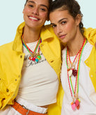 Two people wearing yellow jackets and colorful necklaces against a light blue background