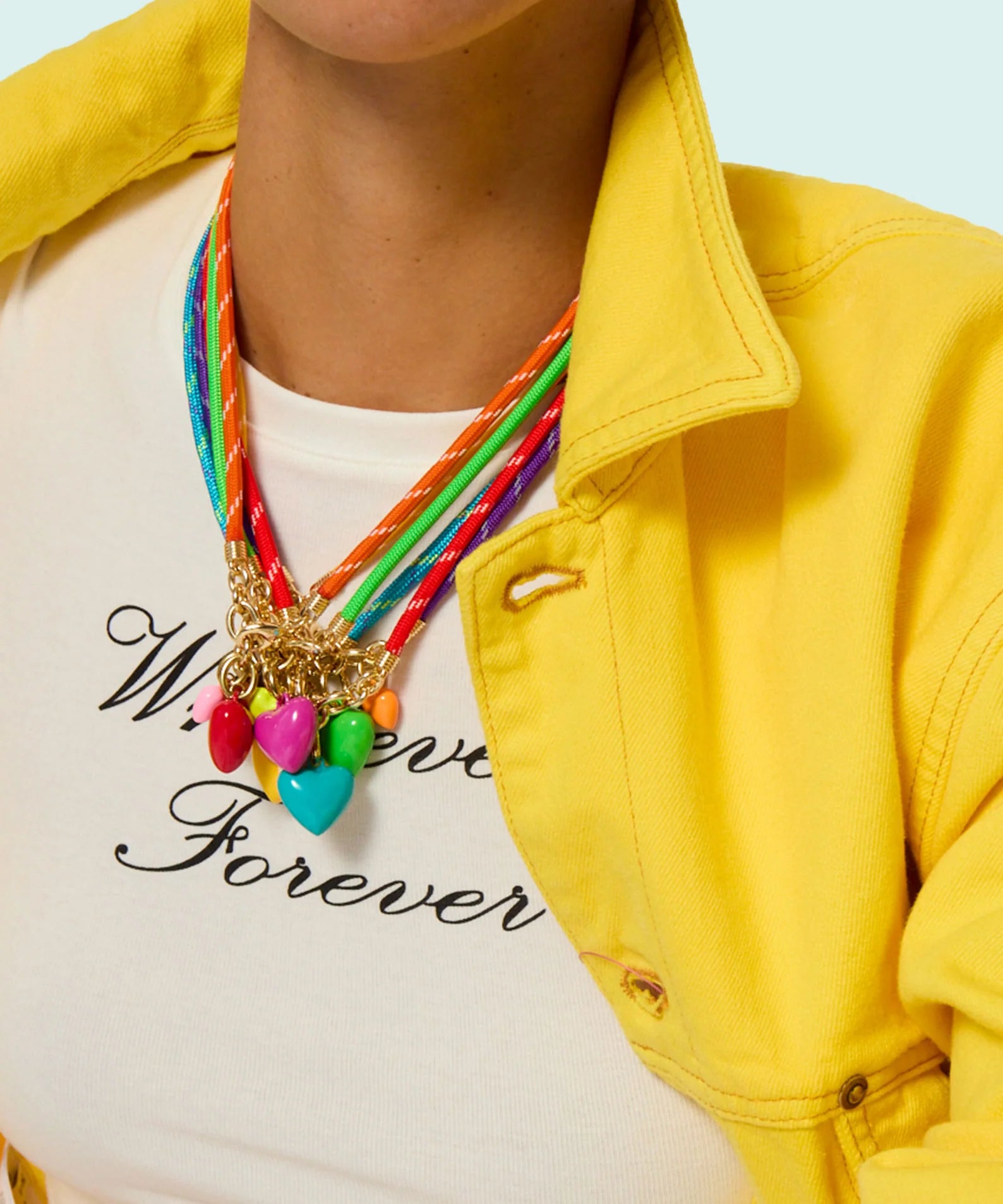 Person wearing a colorful necklace with a yellow jacket and white shirt with text.