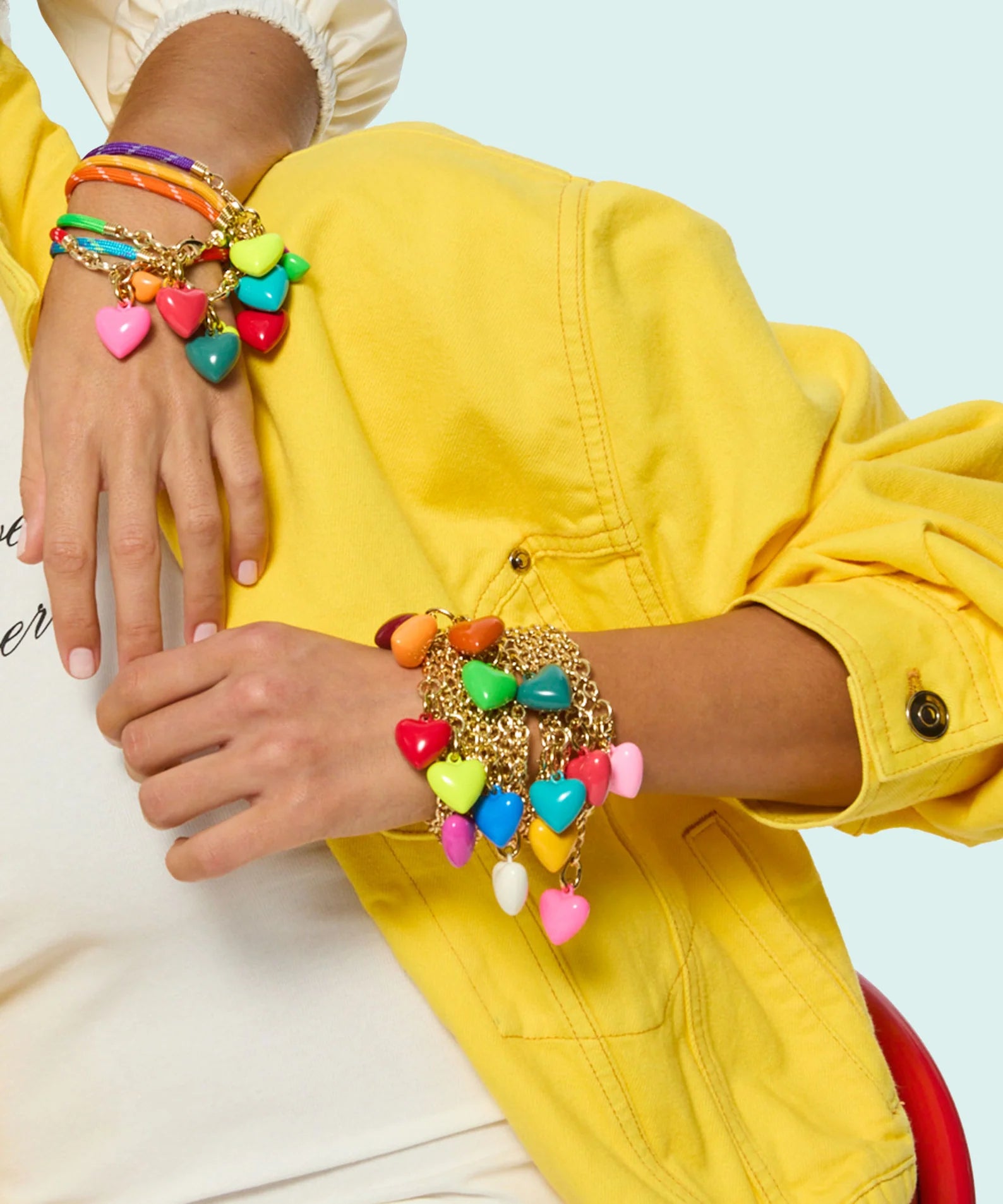 Person wearing a colorful bracelet stack with a yellow jacket and white shirt with text.