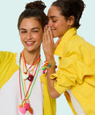Two women wearing colorful necklaces and bracelets against a light blue background