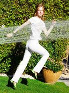 Person in white outfit playing with water from a garden hose in a garden setting