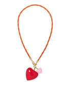 Necklace with a red heart pendant and pink bow on an orange cord against a white background