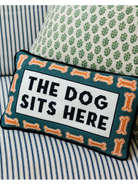 Decorative pillow with 'The Dog Sits Here' text on a striped sofa.
