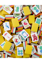 A close-up pile of Mahjong-style tiles with bright yellow backs and white faces decorated with colorful suit symbols and illustrated cards.