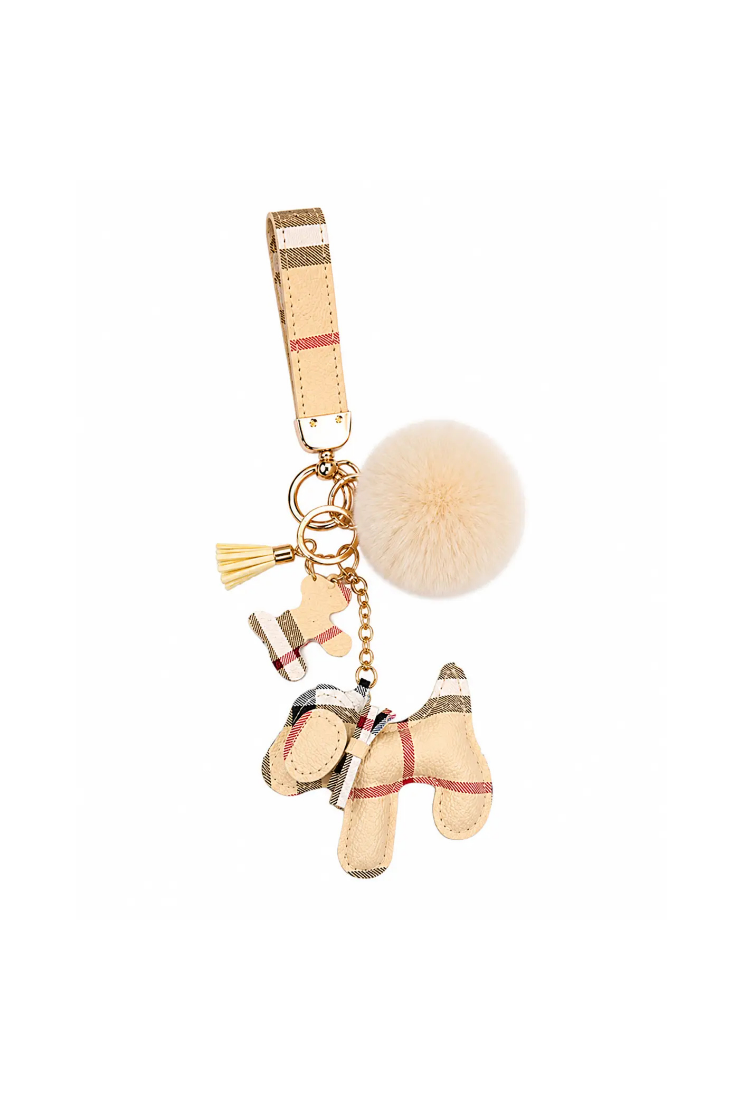 A Burberry-style horse charm keychain featuring a beige check pattern, gold-tone hardware, a small tassel, and a fluffy cream pom-pom on a white background.