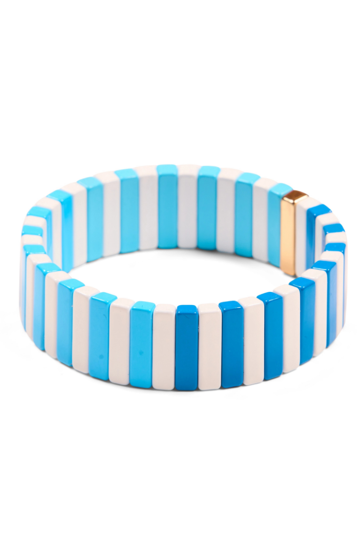 A circular beaded bracelet featuring alternating vertical stripes of light blue, white, and medium blue, with a small gold-toned metal clasp on the side, shown against a plain white background.