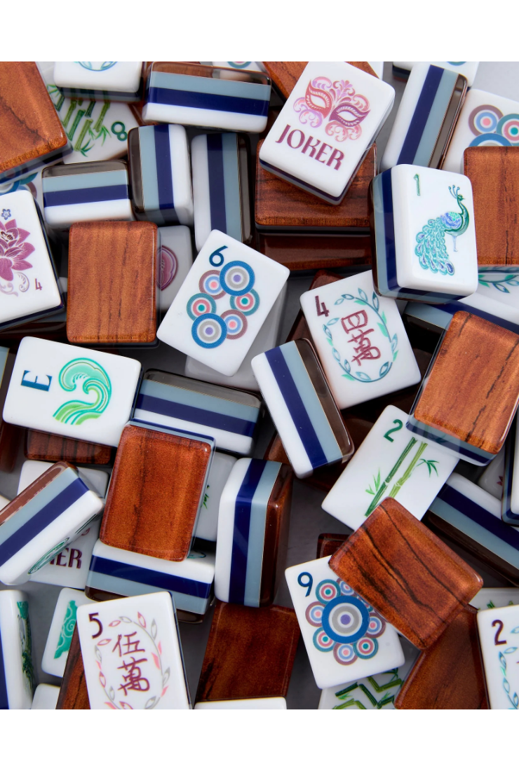 A pile of Mahjong tiles with white faces showing colorful Chinese characters and symbols, paired with wooden backs and striped blue and white borders.