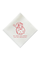 A white textured paper napkin featuring a red line-art illustration of a Santa Claus face and the humorous phrase 'HE SEES YOU WHEN YOU'RE DRINKING' printed below it.