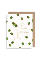 A white greeting card with a gold martini glass illustration, green olives with red pimentos scattered across it, and the phrase 'a tiny bit older' in gold script, shown with a brown kraft envelope on a white background.