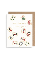 A greeting card with a kraft paper envelope, featuring illustrated mahjong tiles around gold cursive text that reads 'wishing you a lucky year!'.