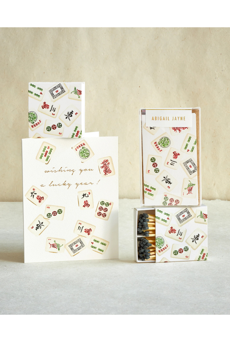 A boxed greeting card set with a white card that reads 'wishing you a lucky year!' and a matching matchbox-style box and smaller card pieces, all decorated with scattered playing card illustrations. The brand name 'ABIGAIL JAYNE' is visible on the front of the box.