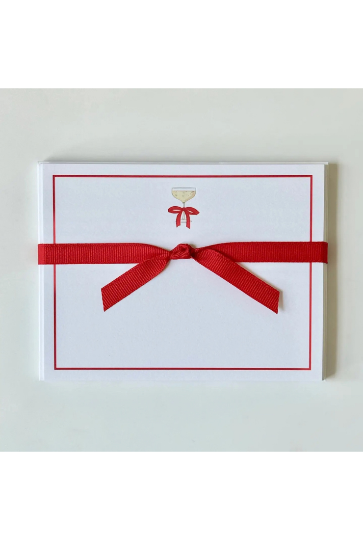 A white rectangular card or envelope with a thin red border, a small gold chalice icon near the top center, and a red ribbon tied around it, photographed on a light neutral background.