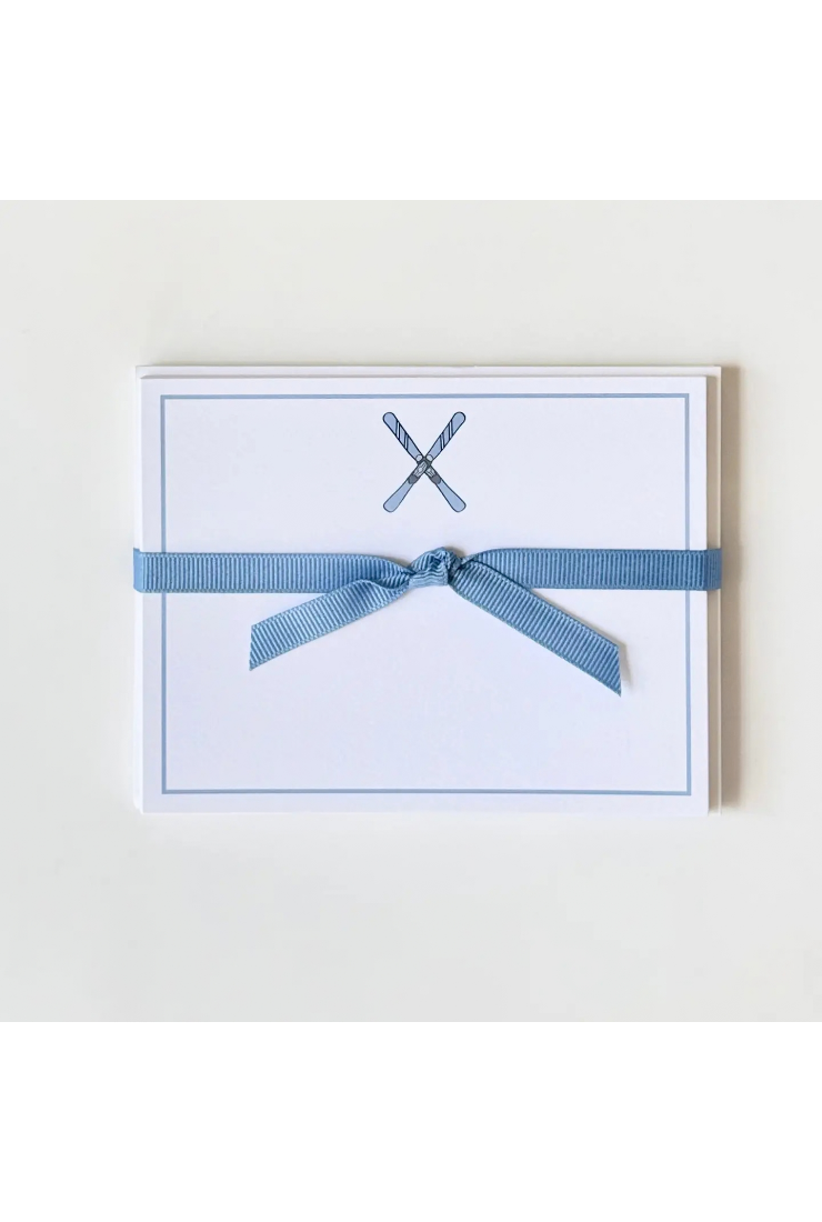 A white rectangular card or envelope with a thin blue border, featuring a small crossed utensil motif near the top and wrapped with a light blue ribbon tied in a bow, shown on a plain light background.