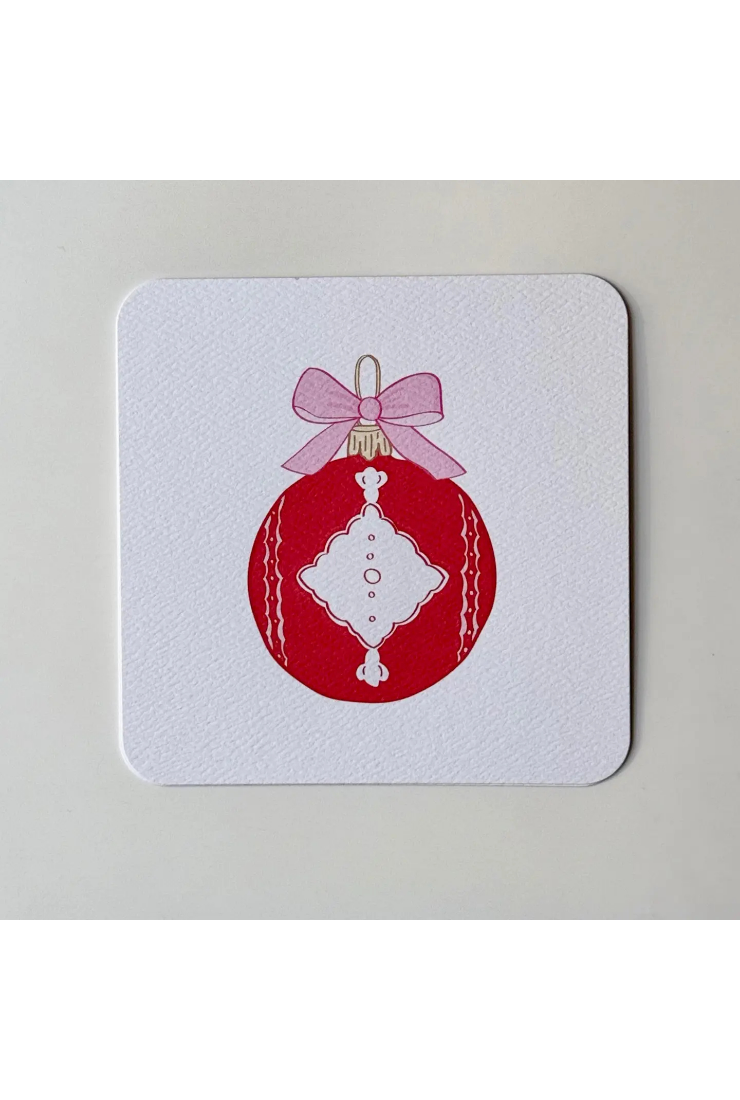 A square white coaster with rounded corners featuring a printed red Christmas ornament design with a pink bow, shown on a light gray background.