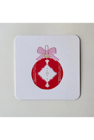 A square white coaster with rounded corners featuring a printed red Christmas ornament design with a pink bow, shown on a light gray background.